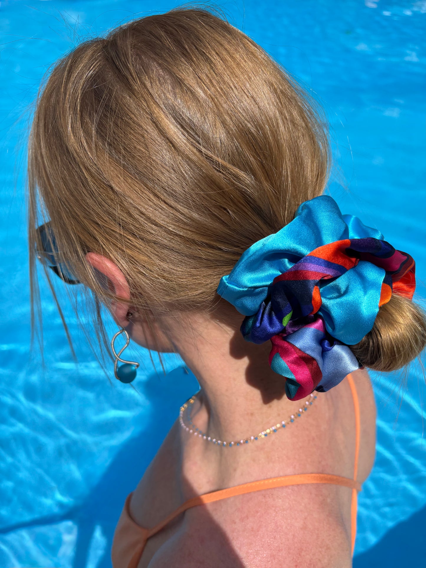 Person with colorful scrunchie duo in hair by a pool