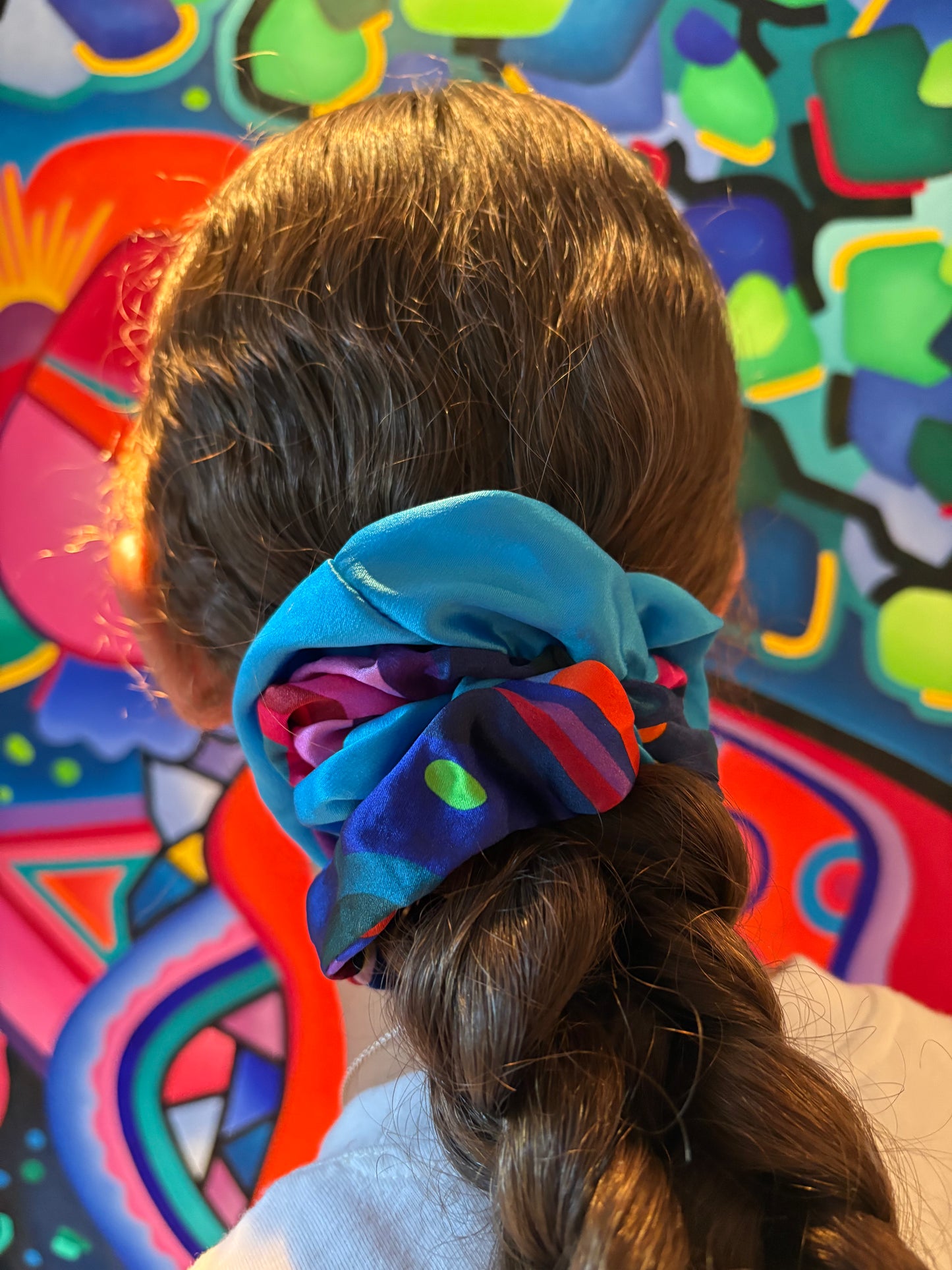 A person with colorful scrunchie duo intheiar hair against a colorful painted background