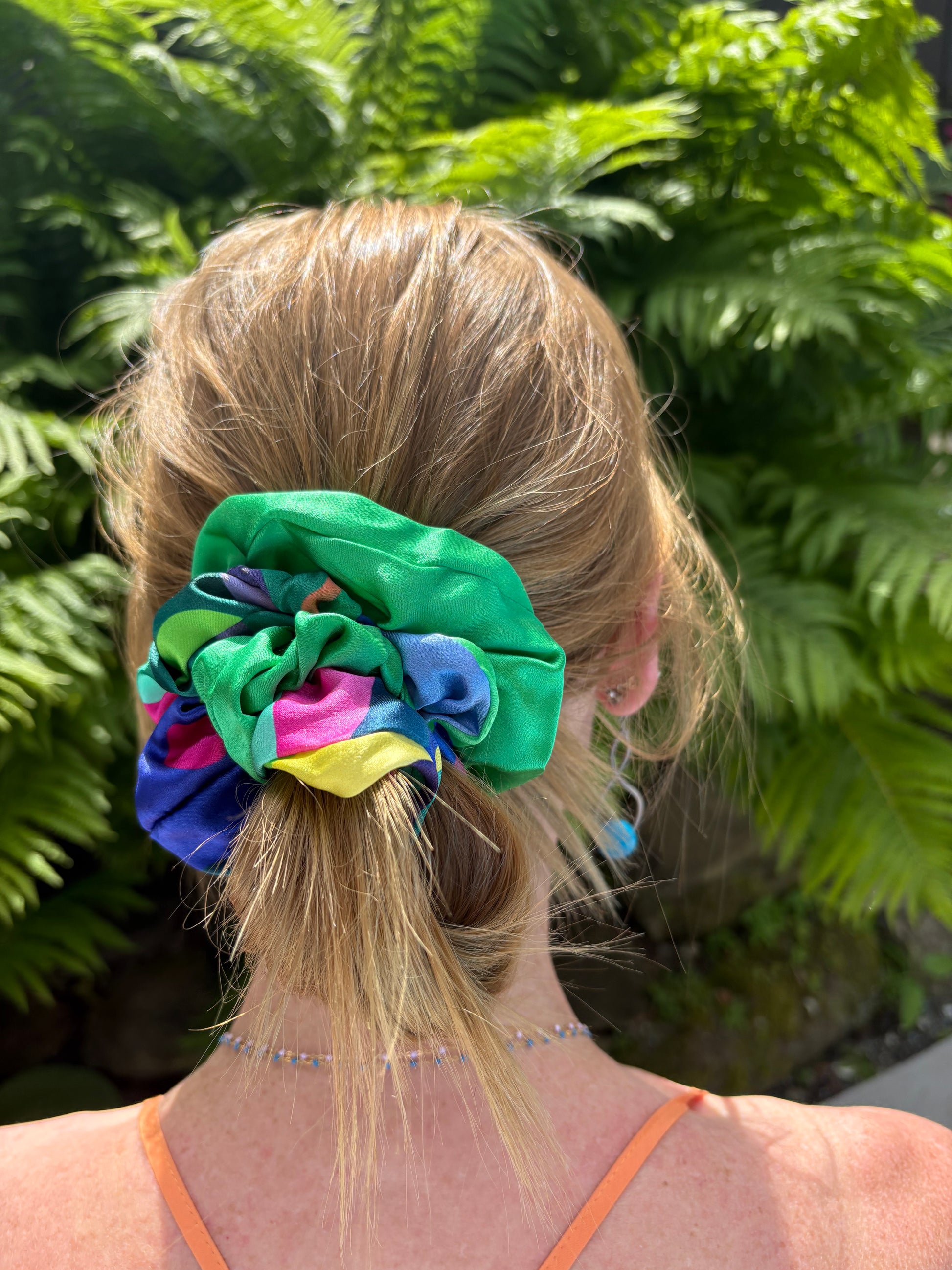 Person with a colorful scrunchie in their hair against a green leafy background
