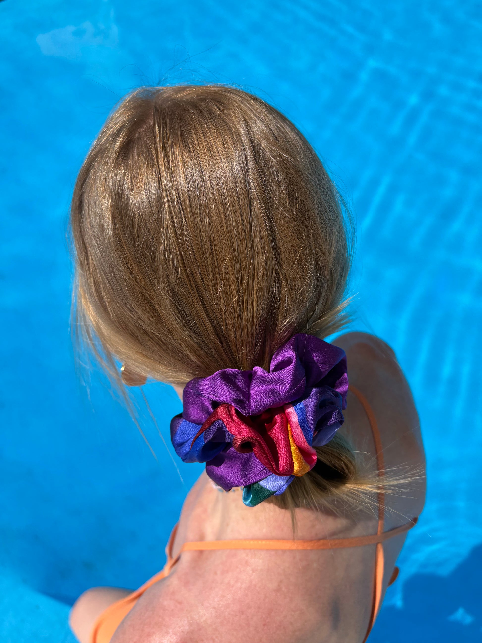 Person with colorful scrunchie duo in their hair against a blue pool background