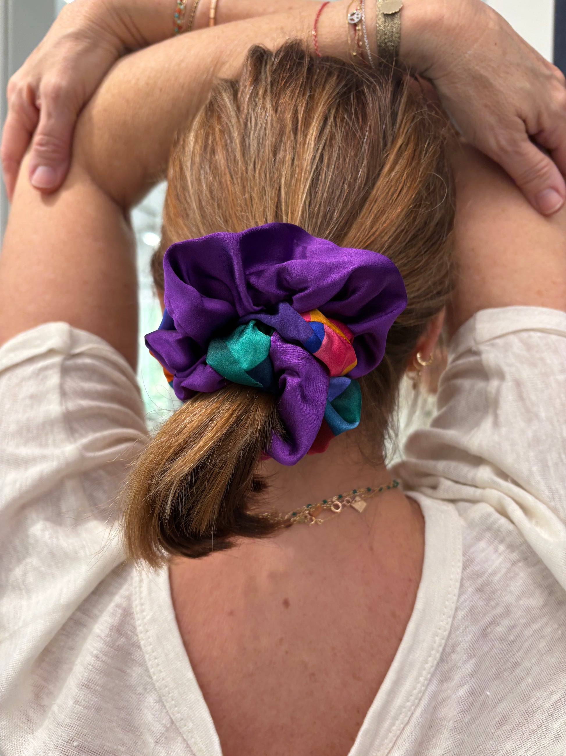 Person with a colorful scrunchie duo in their hair, wearing a white top and bracelets